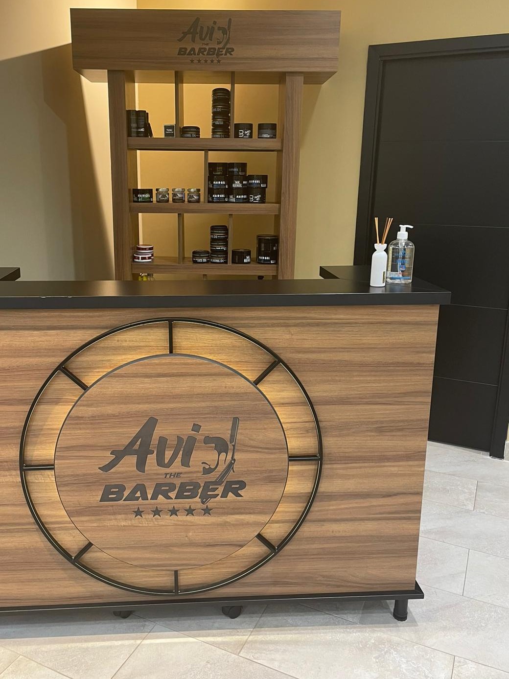 De houten toonbank met het ronde logo van Avi the Barber en de schappen met producten erachter