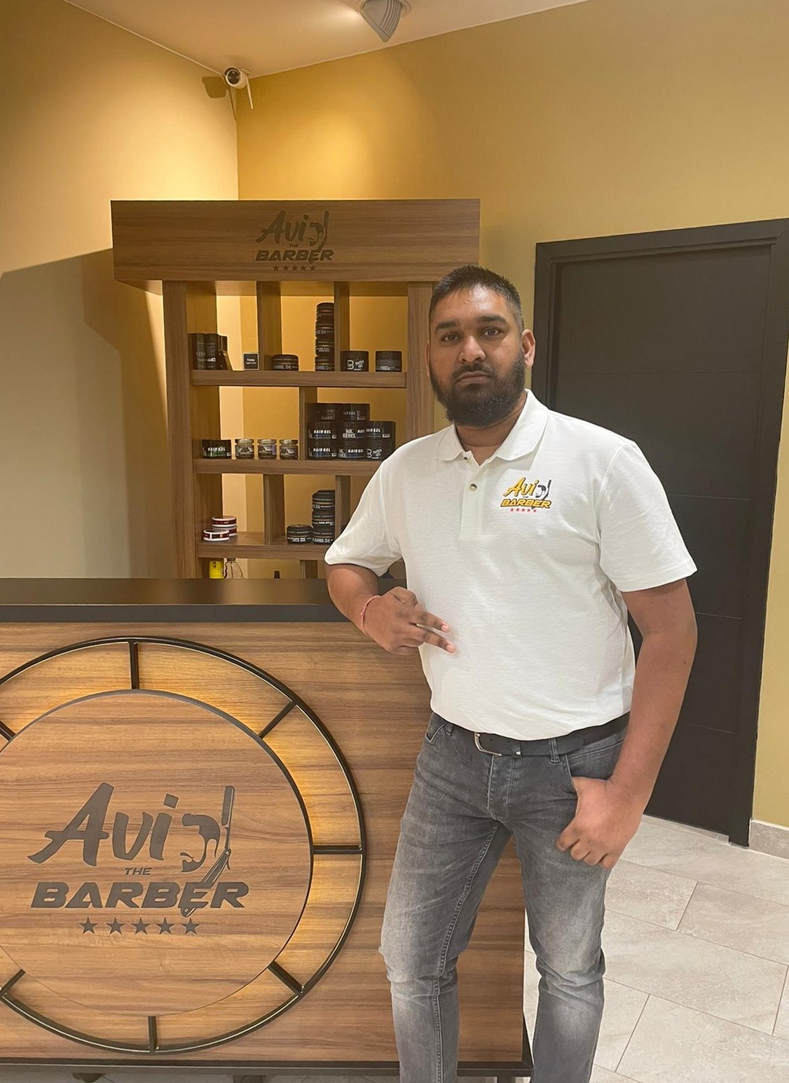 Een man in een wit Avi the Barber-poloshirt leunt op de toonbank