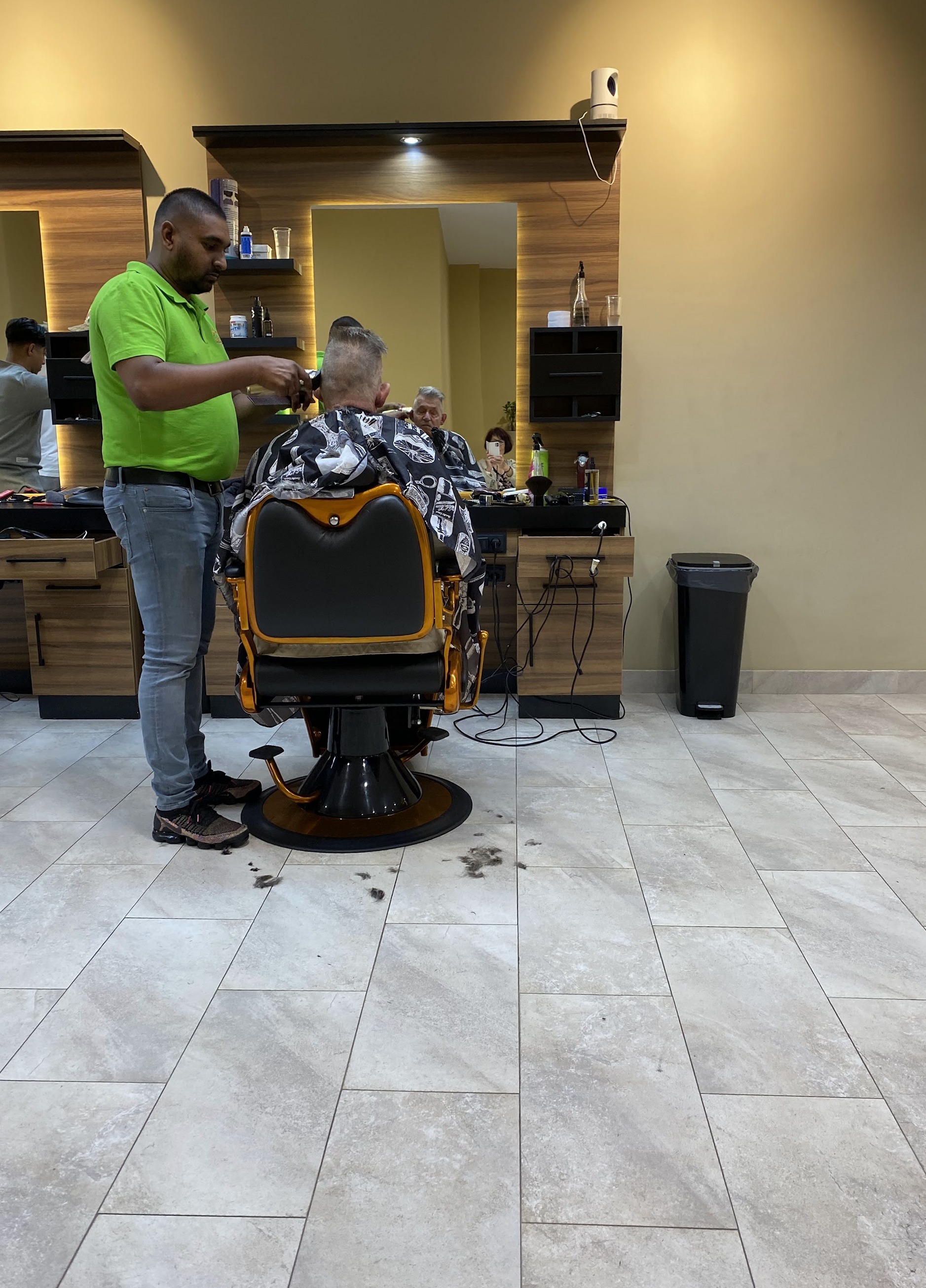 Een barbier in een groen shirt knipt een klant in een van de oranje stoelen